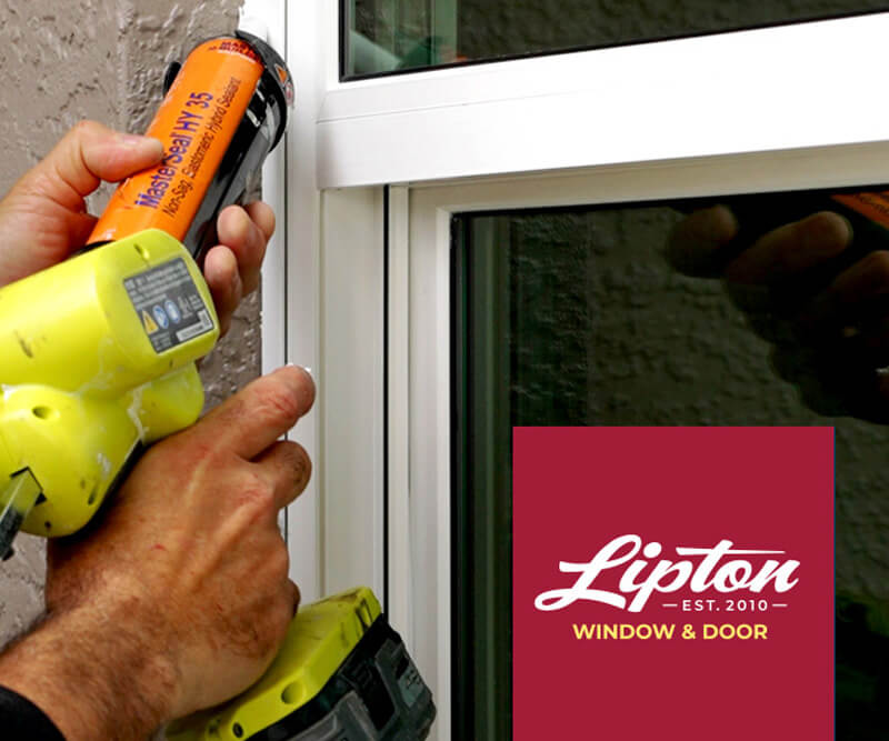 A person using a caulking gun expertly seals the edge of a window frame, showcasing precise window installation techniques. The background features an exterior wall, while the bottom right corner displays a maroon square with Lipton Window &amp; Door Est. 2010 in white.
