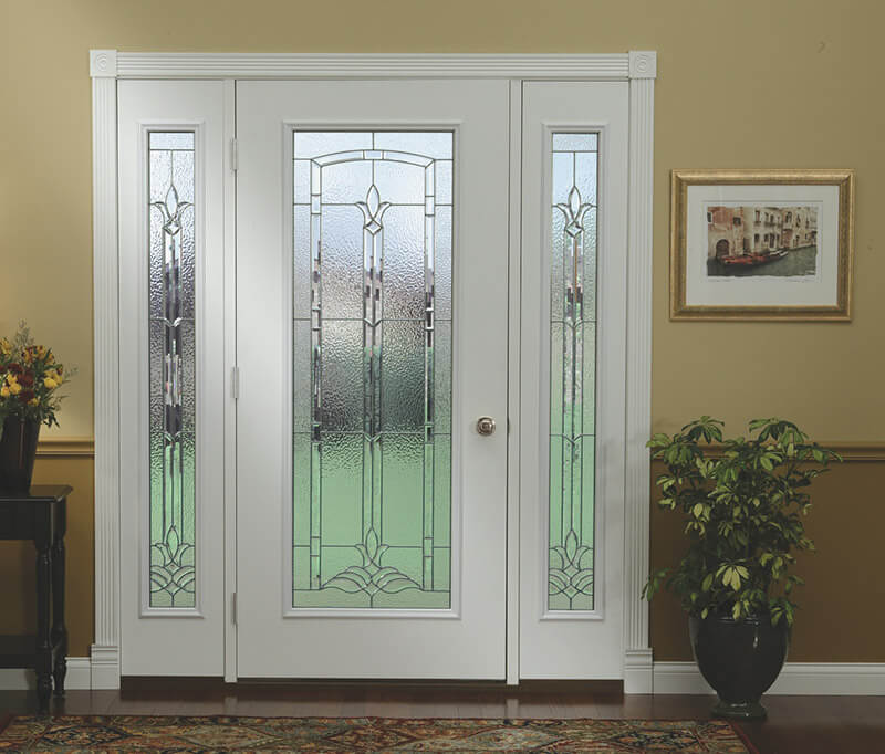 A white front entry door with decorative frosted glass panels is framed by two sidelights of matching design. To the right, a potted plant adds charm, while a framed artwork adorns the beige wall to the left.