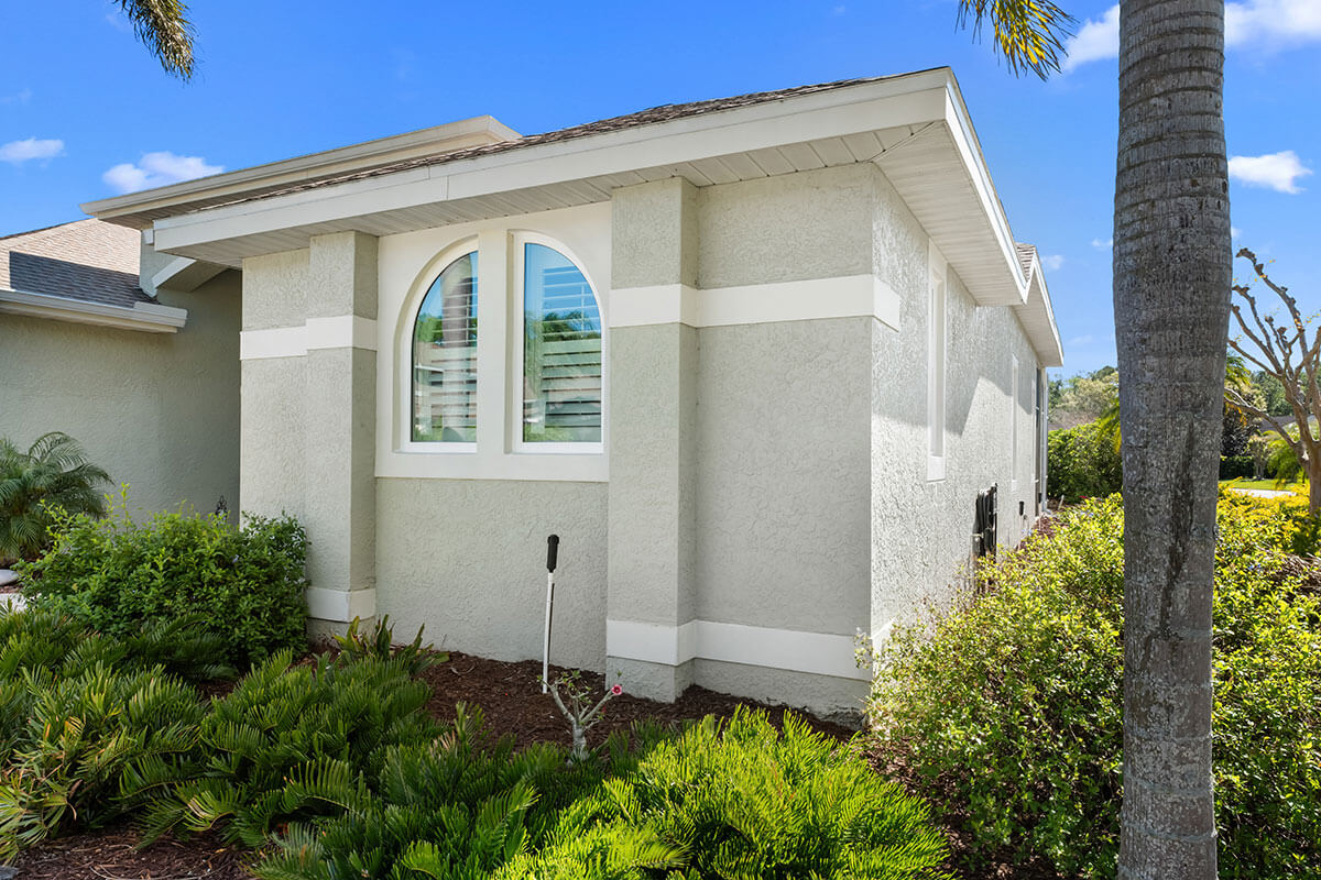 A light gray house with white trim features a large arched replacement shaped window and is surrounded by green shrubs and palm trees under a clear blue Tampa sky.